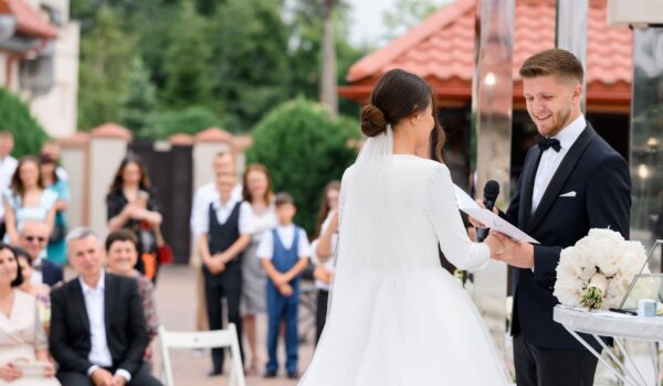 Side view of smiling groom with microphone holding bride's hand on wedding ceremony outdoors